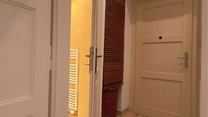 A hallway with a tiled floor, a closed door with a handle, and a partially open door revealing a room with a radiator and a window with blinds. - Apartment with Cathedral View in Hradec Králové (Hradec Králové)