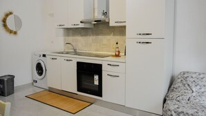 A compact kitchen with a washing machine, dishwasher, and a small countertop with a bottle.