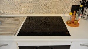 A kitchen with a patterned backsplash, a black induction cooktop, and a white countertop.