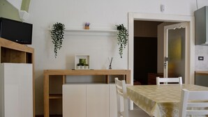 Un petit coin repas comprenant une table, des chaises et une étagère avec des plantes.