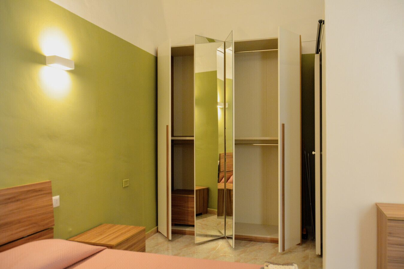 Una stanza con un letto, una testiera in legno, un tavolino, una parete verde, un armadio con uno specchio e un lampadario.