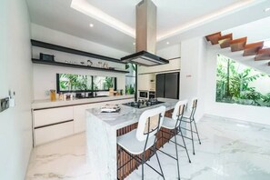 A modern kitchen with a central island, bar stools, and a large window with a view of greenery.