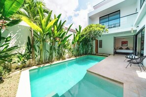 A modern house with a swimming pool surrounded by tropical plants.