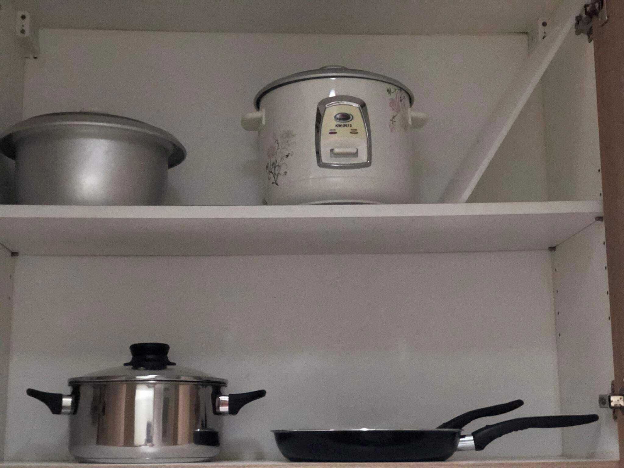 Une étagère de cuisine avec une casserole en acier inoxydable, une casserole émaillée blanche et une poêle noire.