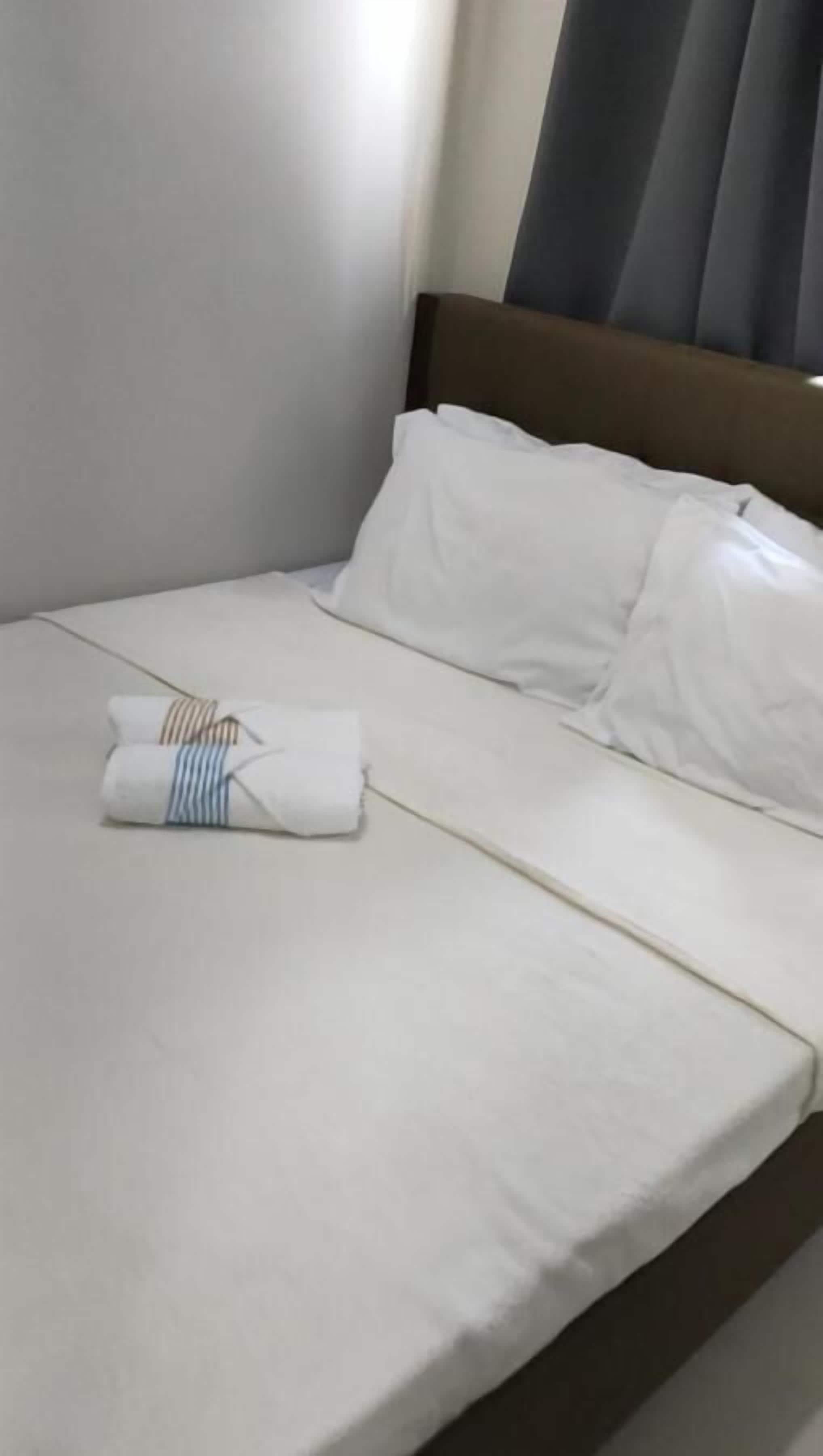 A neatly made bed with white linens and a folded towel with striped patterns.