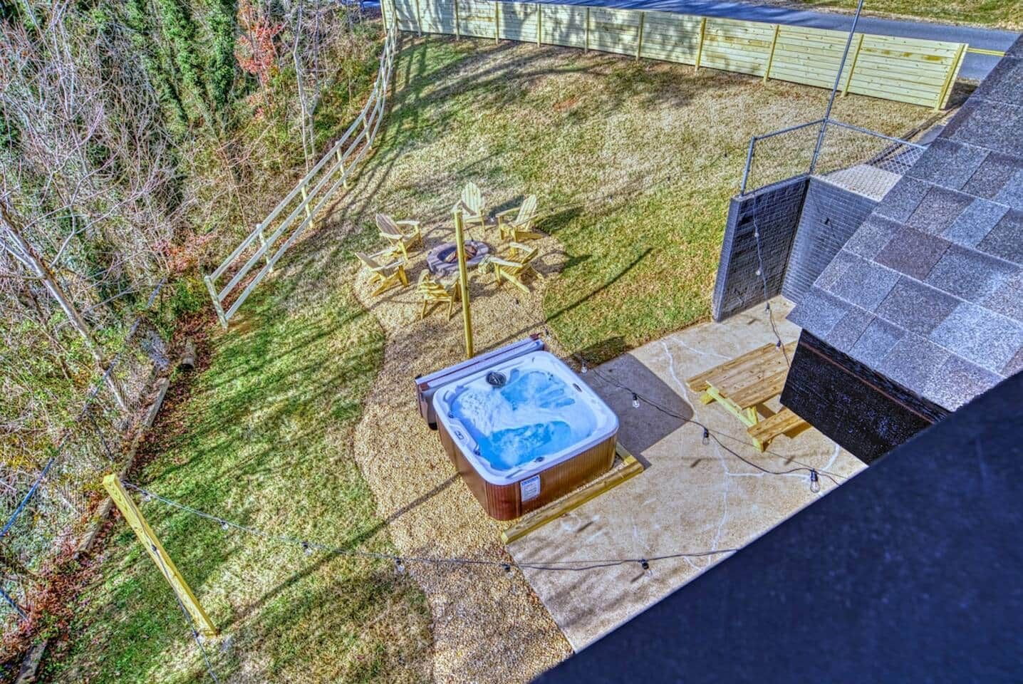 Uma banheira de hidromassagem em um pátio de pedra com deck de madeira e um quintal cercado.