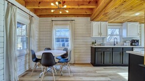 A wooden interior with a dining area, kitchen, and large windows. - The Black Log Cabin - Hot Tub & Game Room (Fredericksburg)