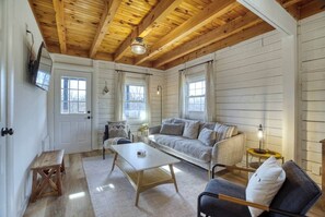 A cozy room with a wooden ceiling, a sofa, a coffee table, and a small table. - The Black Log Cabin - Hot Tub & Game Room (Fredericksburg)