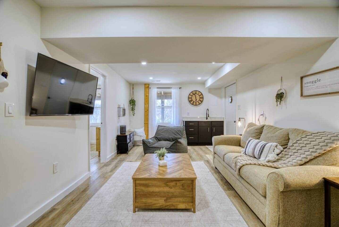 A modern living room with a flat-screen TV, a wooden coffee table, a sofa, and a kitchen area in the background.