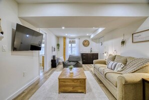 Ein modernes Wohnzimmer mit Flachbildfernseher, Couch, Holztisch und einer Küche im Hintergrund.