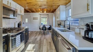 Une cuisine moderne avec un plafond en bois, des appareils en acier inoxydable et un coin repas comprenant une table et des chaises.