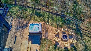 An outdoor patio area with a hot tub, fire pit, and wooden seating. - The Black Log Cabin - Hot Tub & Game Room (Fredericksburg)