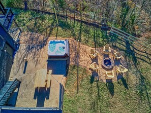 Een terras buiten met een jacuzzi, vuurkuil en houten zitplaatsen.