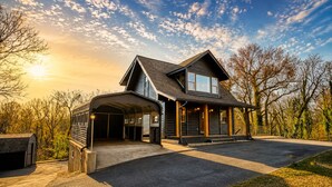 Une cabane en rondins à deux étages, dotée d’un garage fermé, d’une grande allée et offrant une vue magnifique sur les arbres et le ciel.