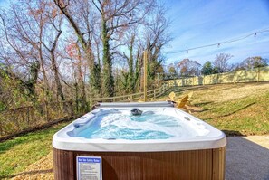 A hot tub outdoors with a safety sign, surrounded by trees and a wooden fence. - The Black Log Cabin - Hot Tub & Game Room (Fredericksburg)