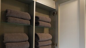 A bathroom with a white sink, a mirror, and a toilet. There are shelves above the sink holding folded towels.