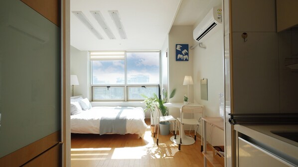 Une chambre d’hôtel moderne dotée d’un grand lit, d’un bureau, d’une chaise et offrant une vue sur la ville grâce à de grandes fenêtres.