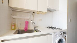A kitchen with a stainless steel sink, a gas stove, and a front-loading washing machine.