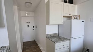Een kleine keuken met witte kasten, een marmeren aanrechtblad en een koelkast.
