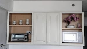 Een keuken met witte kasten, een broodrooster, een magnetron en een plank met een bloempot.