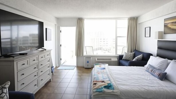 Een hotelkamer met een bed, een televisie, een bureau en een raam met gordijnen.
