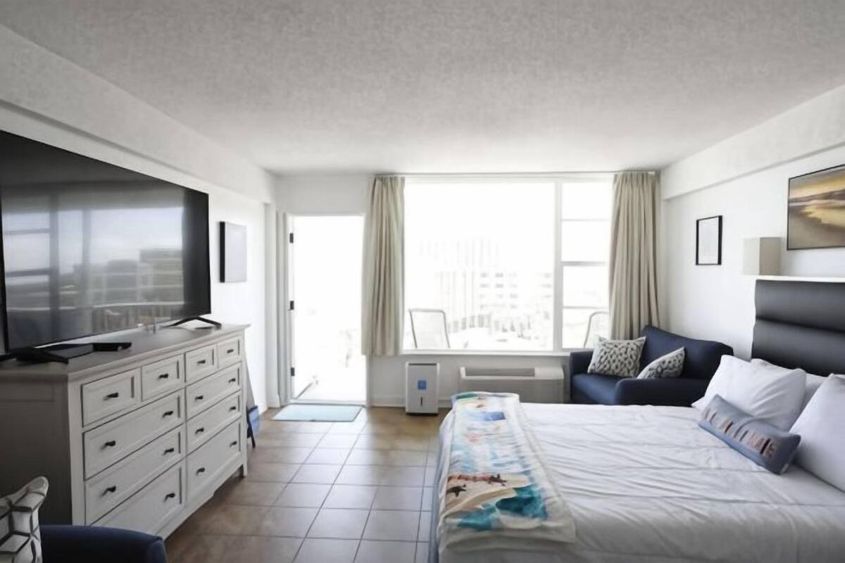 Une chambre d’hôtel avec un lit, une télévision, un bureau et une fenêtre avec des rideaux.