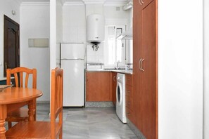 Eine Küche mit Kühlschrank, Waschmaschine und einem Esstisch mit Stühlen.