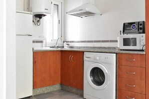 Ett kompakt kök med tvättmaskin, mikrovågsugn och en inbyggd ugn.