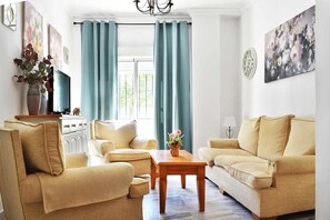 Una sala de estar con sofás color beige, una mesa de centro de madera y un televisor sobre un mueble.