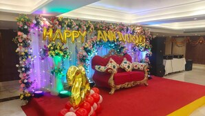 A decorated stage with a red sofa, floral arrangements, and balloons. - Hotel Windsor (Patna)