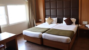 A double bed with a padded headboard, a bedside table, and a window with curtains. - Hotel Windsor (Patna)