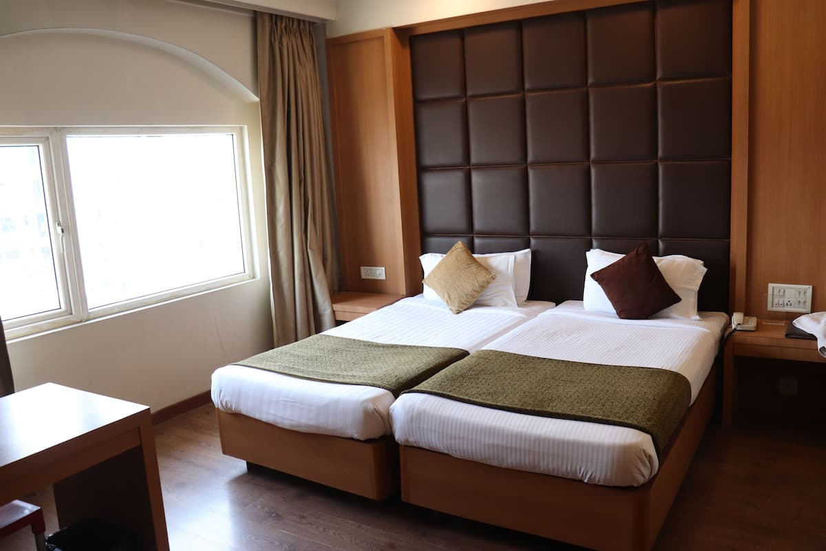 Una cama doble con cabecera acolchada, una mesita de noche y una ventana con cortinas.