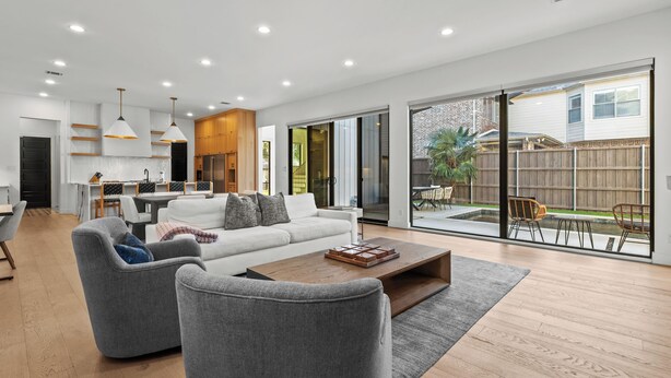 A modern living room with a sofa, armchairs, and a coffee table. There is a dining area with a table and chairs, and a kitchen in the background. - Stunning Modern Farmhouse w/ Pool (Dallas)