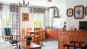 A dining area with a table and chairs, a kitchen with cabinets and a stove, and a living area with a sofa and a TV.