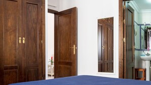 A bedroom with a large bed, wooden wardrobe, and a bathroom with a mirror and sink.