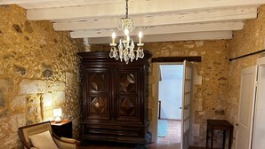 Una habitación con paredes de piedra, una araña, un aparador de madera, un sofá y una cama.