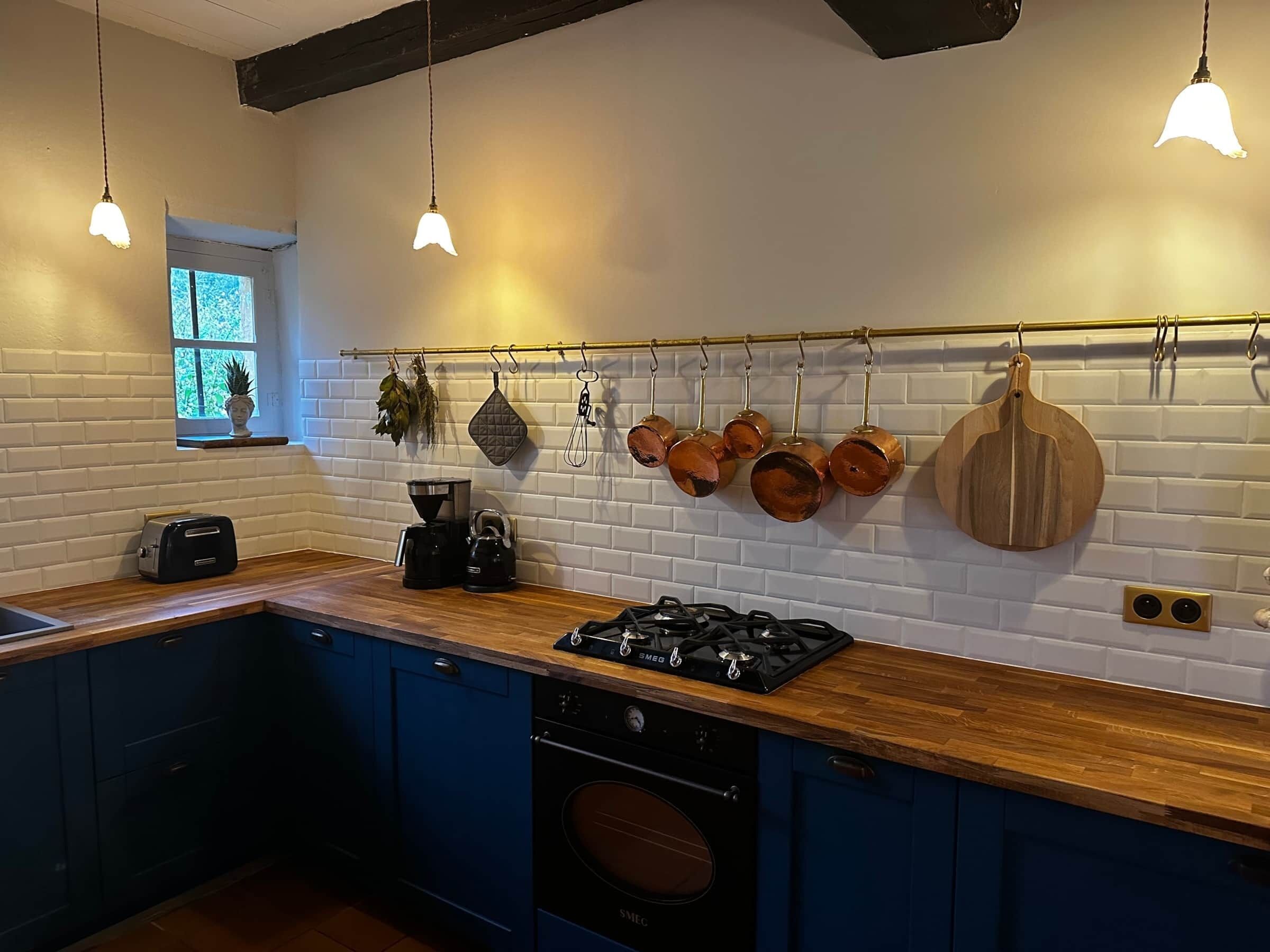 A modern kitchen with blue cabinets, a wooden countertop, a gas stove, a coffee maker, and hanging copper pots.