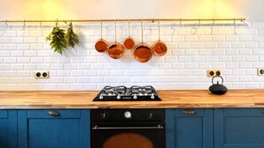 Una cocina con salpicadero de ladrillo blanco, armarios azules, encimera de madera, estufa a gas, horno, ollas colgantes y luces colgantes.