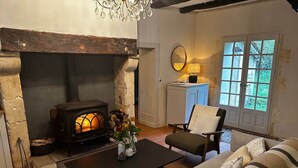 Un salón acogedor con chimenea de piedra, una mesa de madera, un sofá y vistas a la vegetación a través de una ventana.
