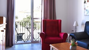 Una habitació amb una cadira vermella, un sofà blau, una taula de fusta amb una planta i un balcó amb taula i cadires.