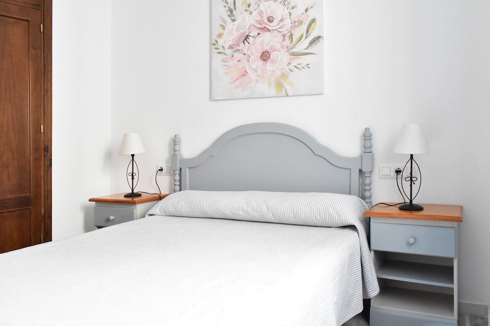 Une chambre à coucher comprenant un lit, deux tables de chevet, une commode, une armoire en bois et un tableau floral accroché au mur.