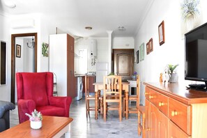 Un salón con un sillón rojo, una mesa de comedor de madera y un televisor sobre un mueble de madera.