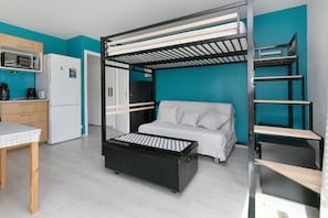 Une petite chambre comprenant un lit superposé, un coin cuisine et une petite table.