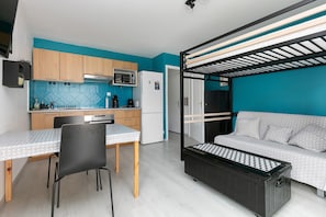 A compact living space with a kitchenette, a dining area, a sofa, and a bunk bed.