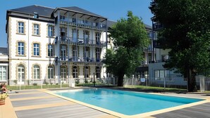 Una piscina con bordo in legno, circondata da un edificio a più piani con balconi.