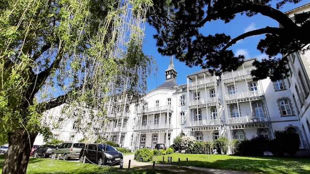 Un edificio a più piani con balconi, una torre e un prato curato.