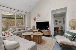 Een moderne woonkamer met een bank, twee ronde salontafels, een flatscreen-tv en een stenen muur.
