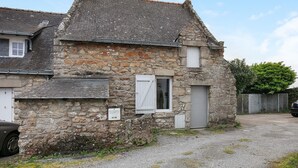 Un bâtiment en pierre avec un toit en pente, une petite fenêtre avec des volets et une porte de garage.