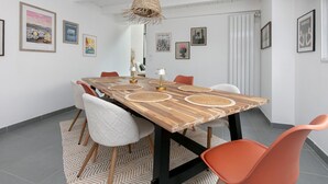 Un coin repas avec une table en bois, des chaises orange et un luminaire suspendu en fibres tressées.