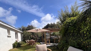 Un espace patio doté d’un sol en pierre, d’un canapé blanc, d’un fauteuil beige et d’une table en bois.